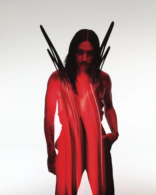 Fashion portrait of a person with long dark hair, mustache, tattoos, wearing a sleeveless shirt with graphic red digital effect.