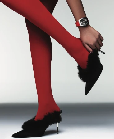 Woman in red tights and black high-heeled shoes with fur accents poses against a pale background, showcasing fashion and style.
