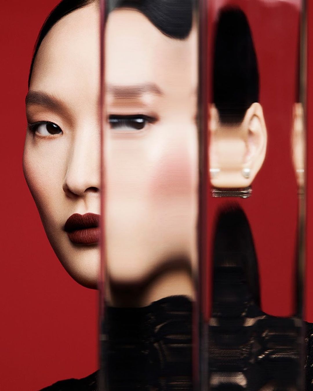 Close-up studio shot of an Asian female model with dark red lipstick, partly visible through vertically arranged reflective glass.