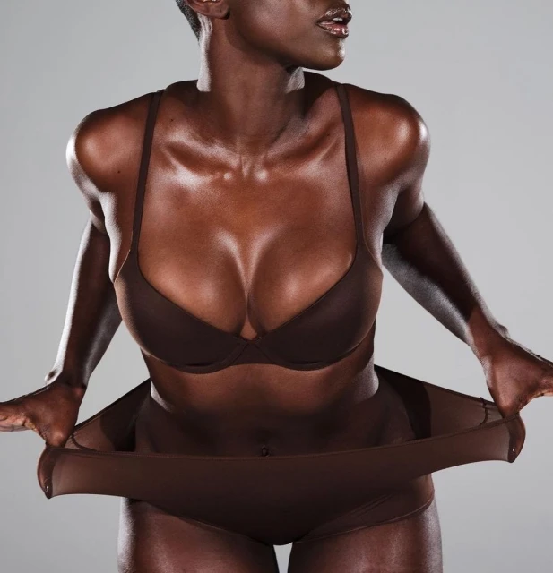 Striking studio shot of a fit Black woman in underwear, holding the elastic waistband with both hands, against a grey backdrop.