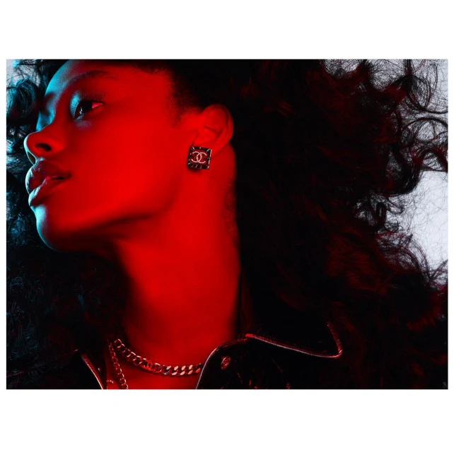Profile shot of a woman with curly dark hair wearing a black leather jacket and gold chain. Red and blue lighting illuminates the scene.