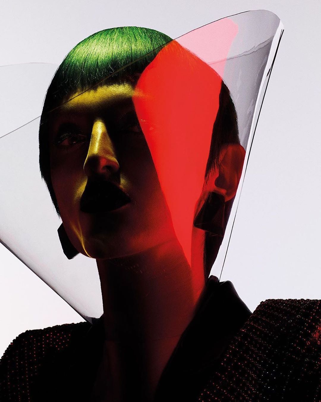 Fashionable woman with green hair poses in a studio with creative lighting and clear transparent material over her head and shoulders.