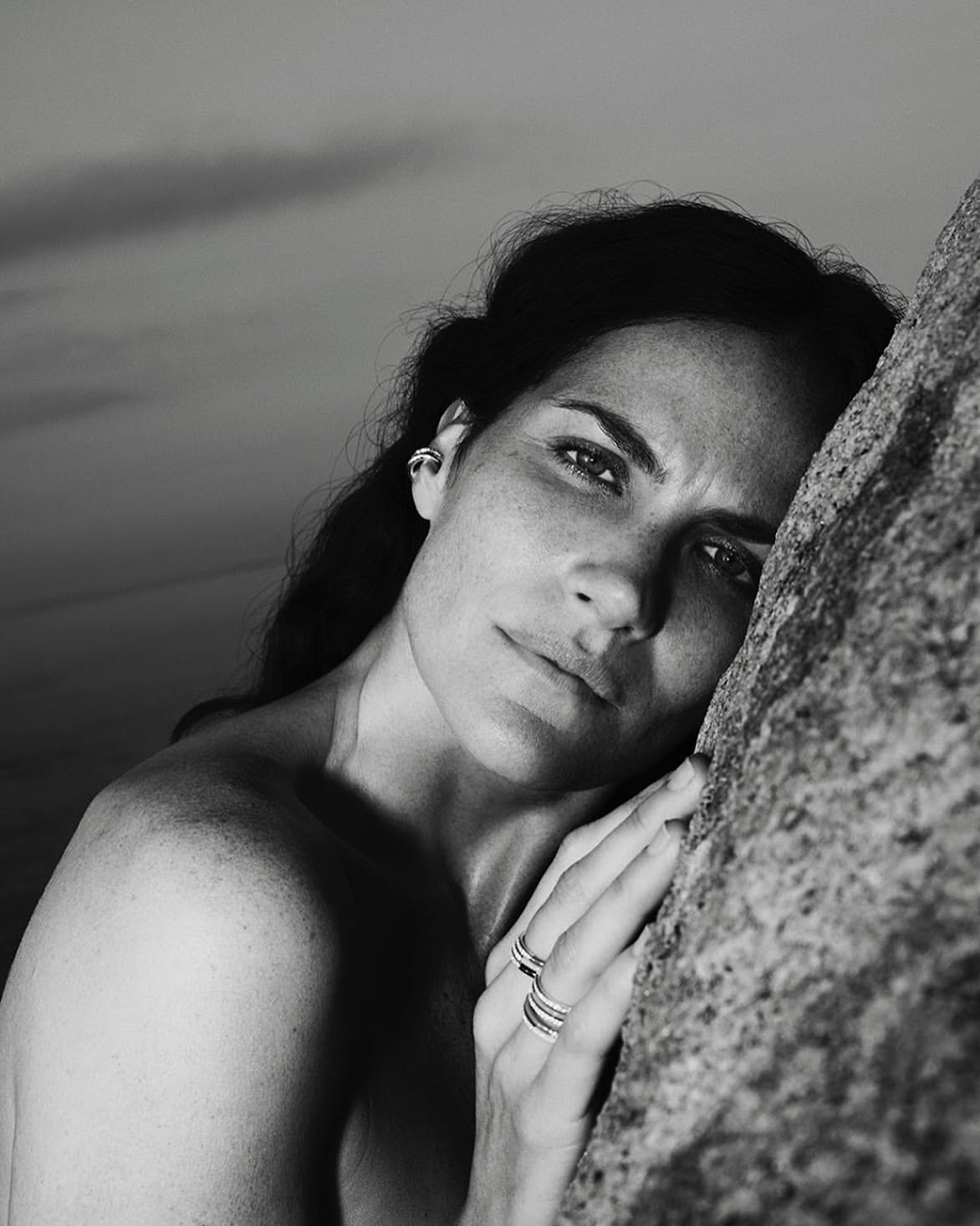 Close-up monochrome portrait of a woman resting her face against a textured rock surface, wearing rings.