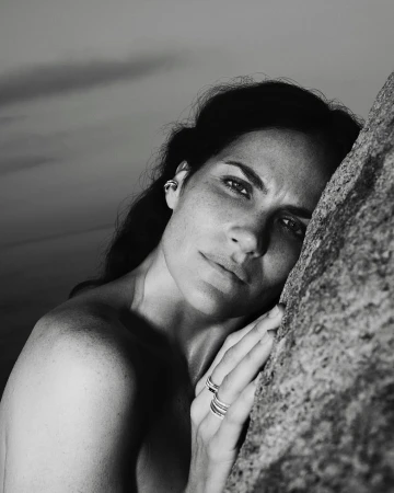 Close-up monochrome portrait of a woman resting her face against a textured rock surface, wearing rings.
