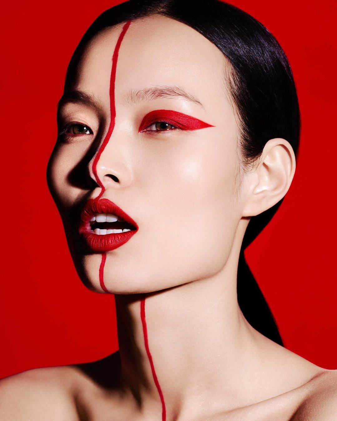 Striking beauty shot of an Asian woman with red lipstick and creative red eyeliner against a solid red background, studio lighting.