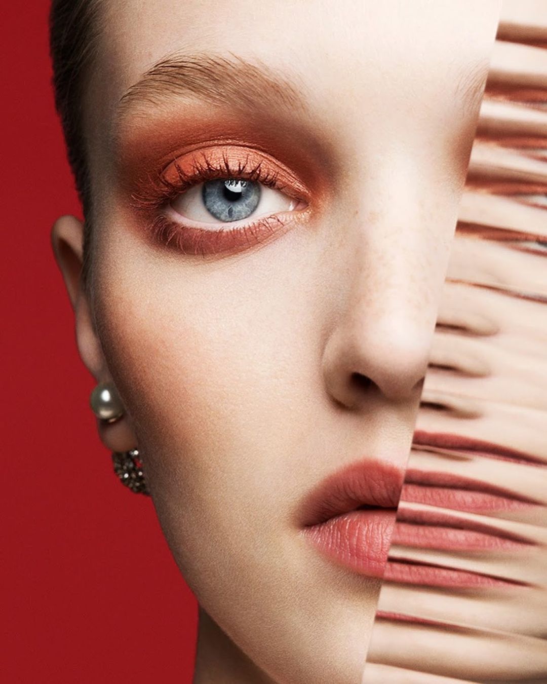 Close-up portrait of a woman with warm eyeshadow and blue eyes against a bold red background by Ben Hassett