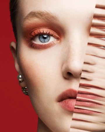 Close-up portrait of a woman with warm eyeshadow and blue eyes against a bold red background by Ben Hassett
