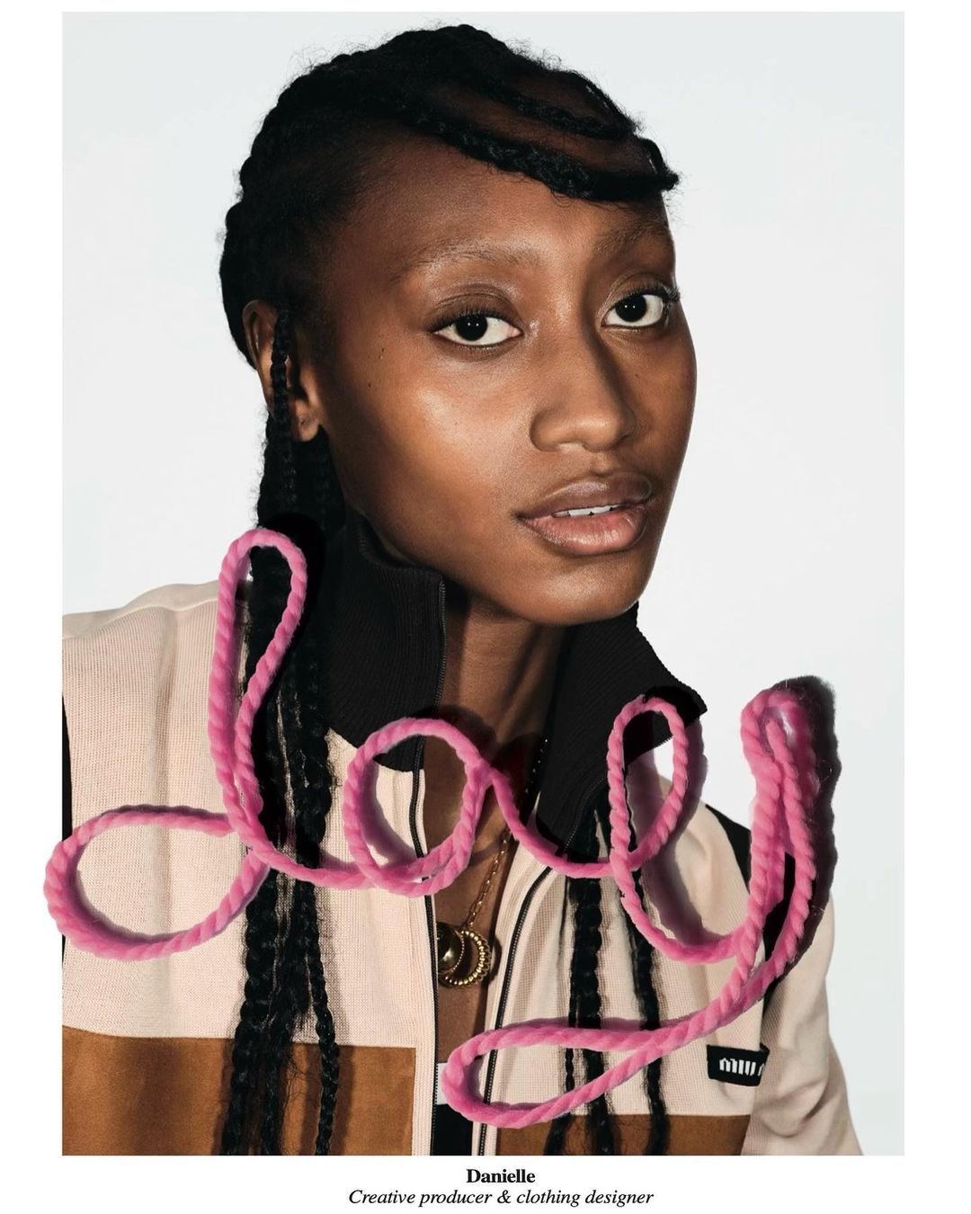 Portrait of an African-American woman with dark braided hair, wearing a jacket with a tan and brown pattern, against a white background.