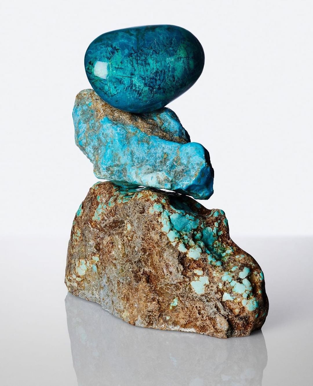 Close-up studio shot of a stack of blue and brown gemstones with a polished turquoise top stone, against a gradient white background.
