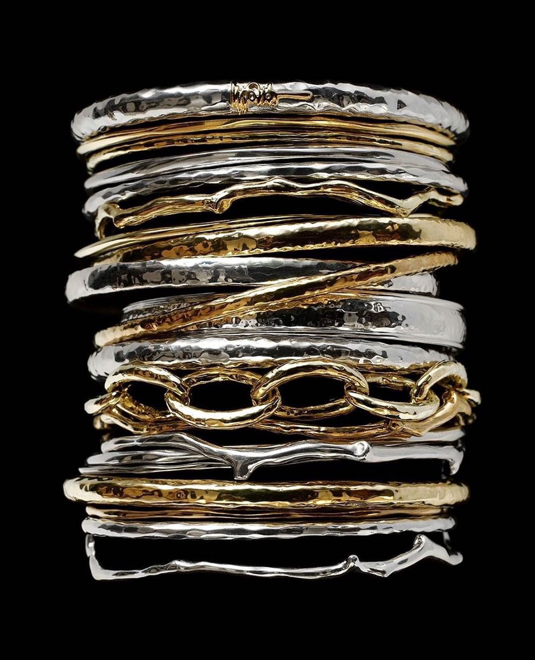 Stack of gold and silver hammered bangles are featured against a black backdrop in this studio shot, showcasing textures and shine.