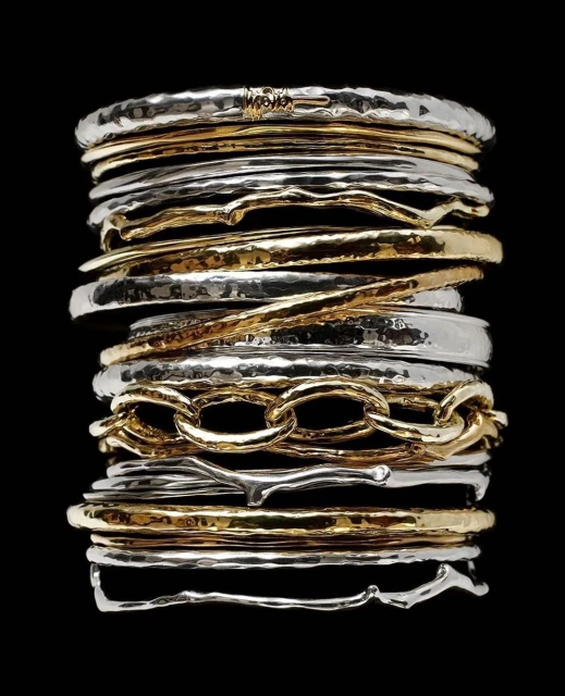 Stack of gold and silver hammered bangles are featured against a black backdrop in this studio shot, showcasing textures and shine.