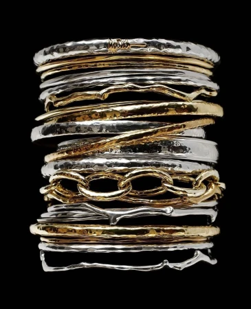Stack of gold and silver hammered bangles are featured against a black backdrop in this studio shot, showcasing textures and shine.
