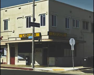 Two-story liquor store building with signage, visible windows, and a street sign on a pole in an urban setting during daylight.