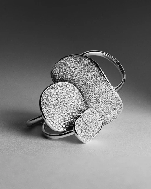 Close-up of a textured, geometric silver ring featuring a square, oval, and organic shape, set against a neutral gray gradient background.