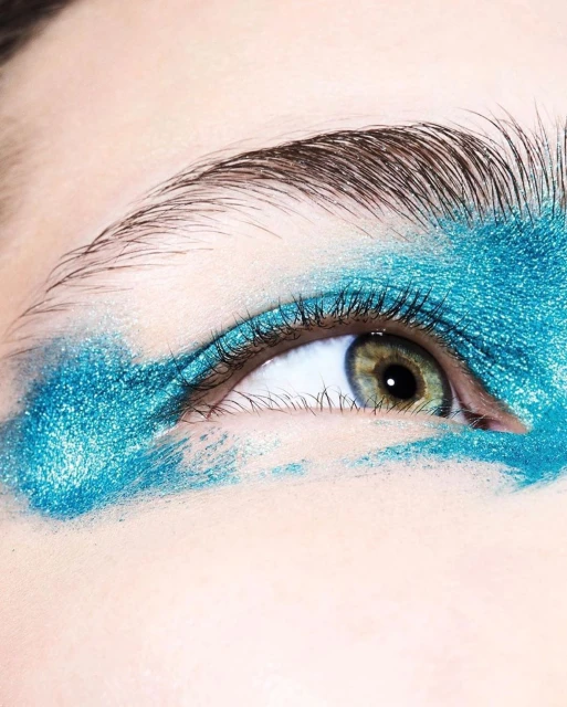 Extreme close-up of a person's eye with iridescent teal eyeshadow applied on the lid and under the eye in a diffused manner.