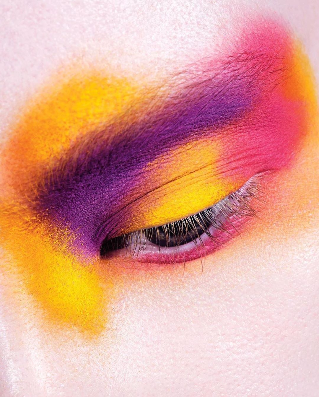 Close-up of an eye with colorful makeup in shades of purple, pink, and yellow, showcasing vibrant cosmetic art and beauty.