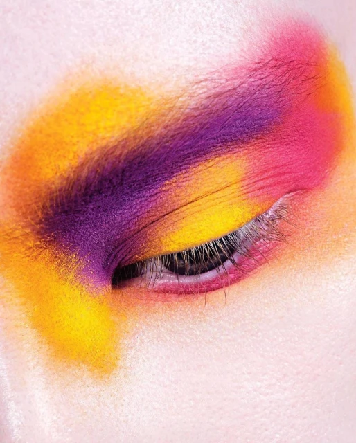 Close-up of an eye with colorful makeup in shades of purple, pink, and yellow, showcasing vibrant cosmetic art and beauty.
