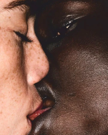 Close-up portrait of two faces of different skin tones, one light with freckles and one dark, very close together, almost kissing.