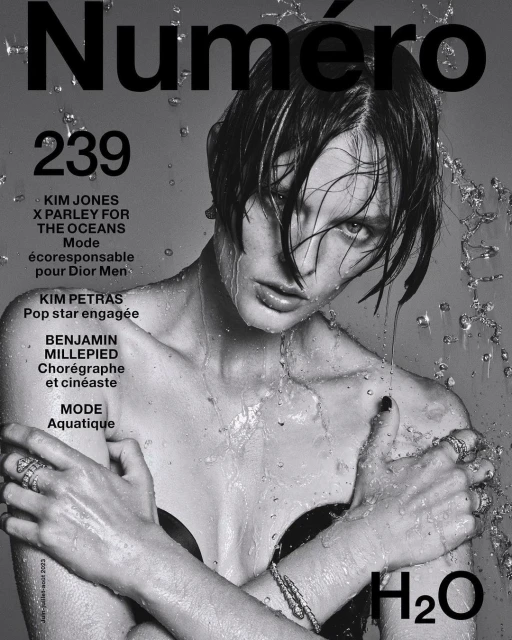 Black and white magazine cover featuring a model with wet hair and water droplets, adorned with jewelry and minimal clothing, H2O text.