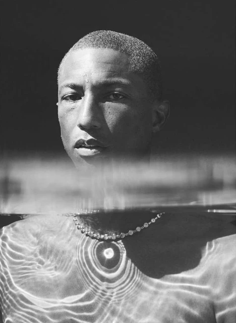Monochrome portrait of adult male partially submerged in water with jewelry, the water reflecting light patterns on his body.