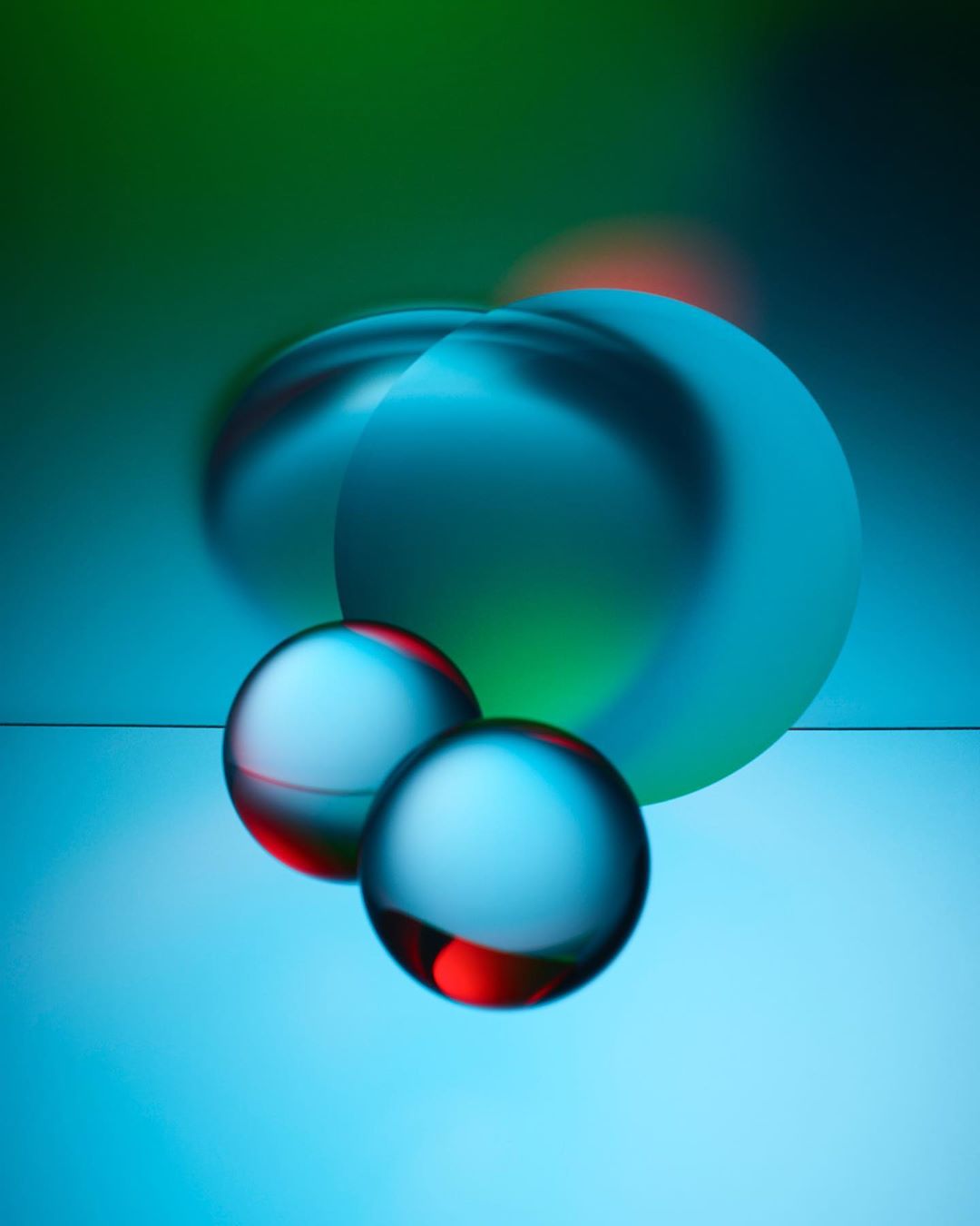 Abstract still life featuring blue and red glass spheres against a graduated green and blue background with blurred lighting effects.
