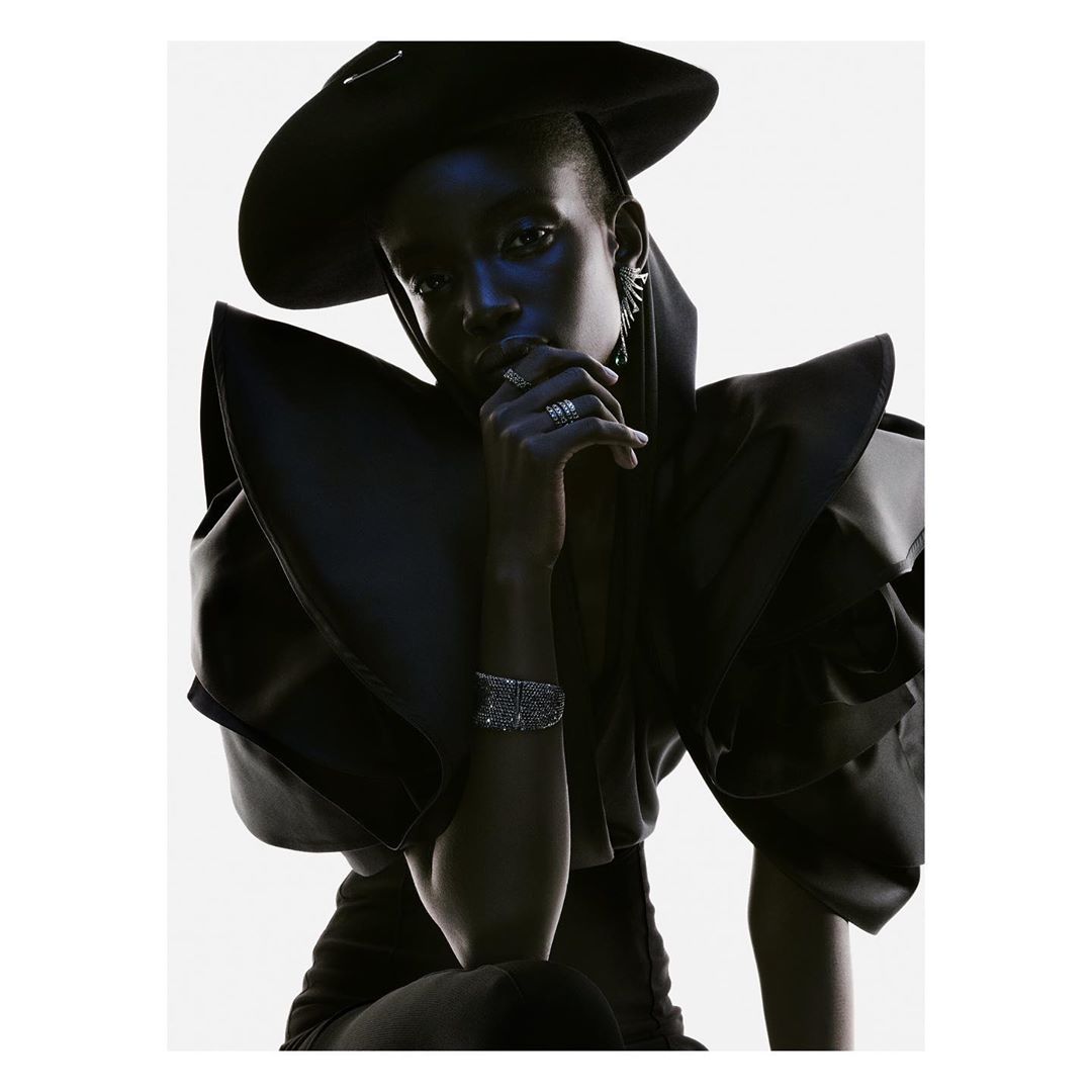 Dramatic high-fashion portrait of an African-American woman wearing a black hat and sculptural clothing with silver rings and bracelet.