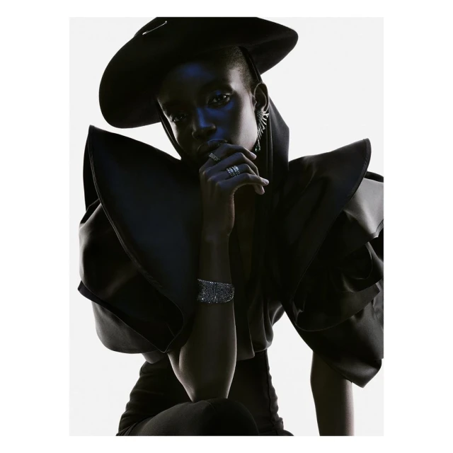 Dramatic high-fashion portrait of an African-American woman wearing a black hat and sculptural clothing with silver rings and bracelet.