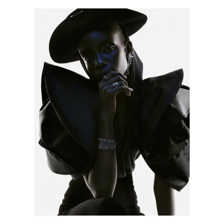 Dramatic high-fashion portrait of an African-American woman wearing a black hat and sculptural clothing with silver rings and bracelet.