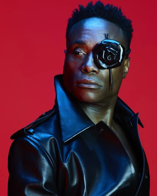 Close-up portrait of an adult male wearing a black leather trench coat and a black rose accessory over one eye on a red background.