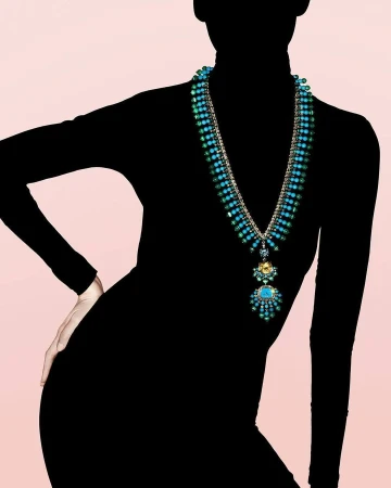 Model wearing black turtleneck and elaborate turquoise gemstone necklace against a pink backdrop