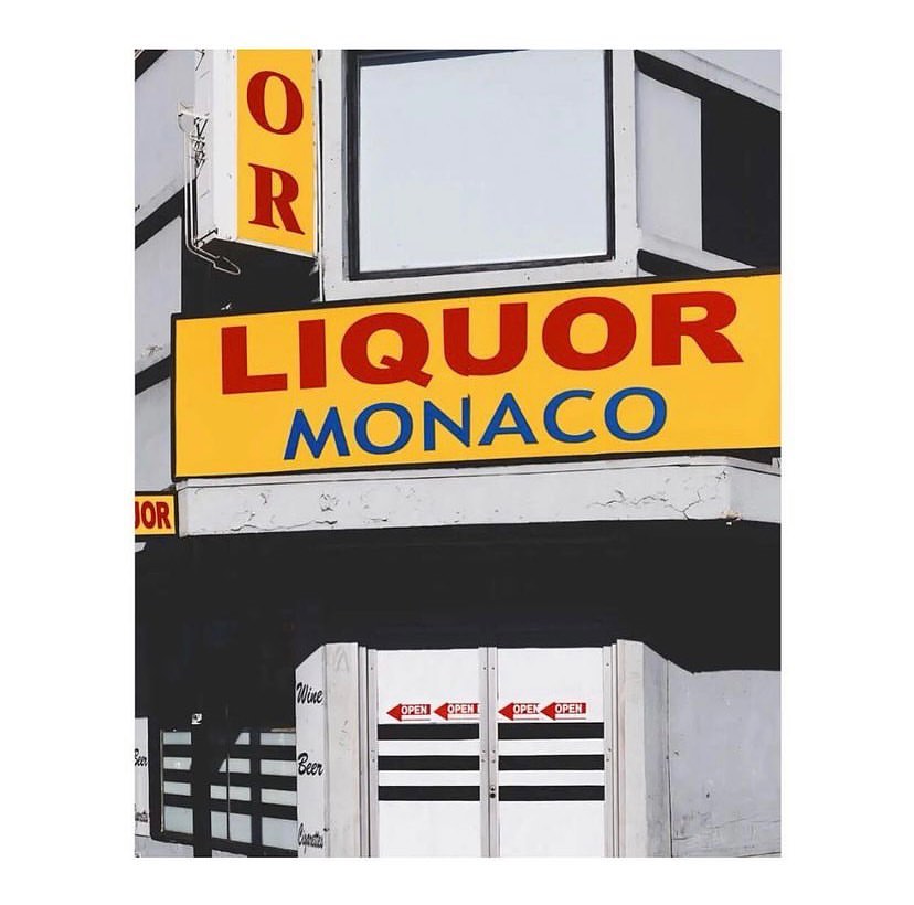 Eye-level shot of a liquor store exterior with a yellow sign reading 'Liquor Monaco' above a white door with black stripes.