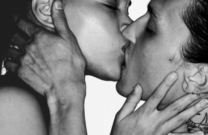 Close-up black and white photo of two people kissing, with one person's hand gently holding the other's face and neck.
