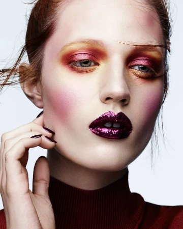 Close-up portrait of a woman with vibrant pink and yellow eyeshadow and glittering purple lipstick photographed by Ben Hassett.