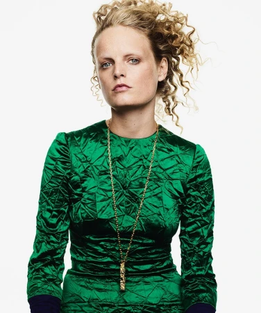 Portrait of a woman with curly blonde hair wearing a textured green long-sleeve dress and a long gold necklace