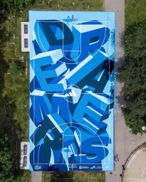 Aerial view of a brightly painted blue outdoor basketball court featuring large 3D typography across the surface.