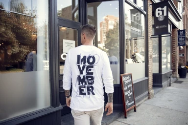 Man from behind wearing a white long-sleeve t-shirt with bold typography walking toward a storefront in New York