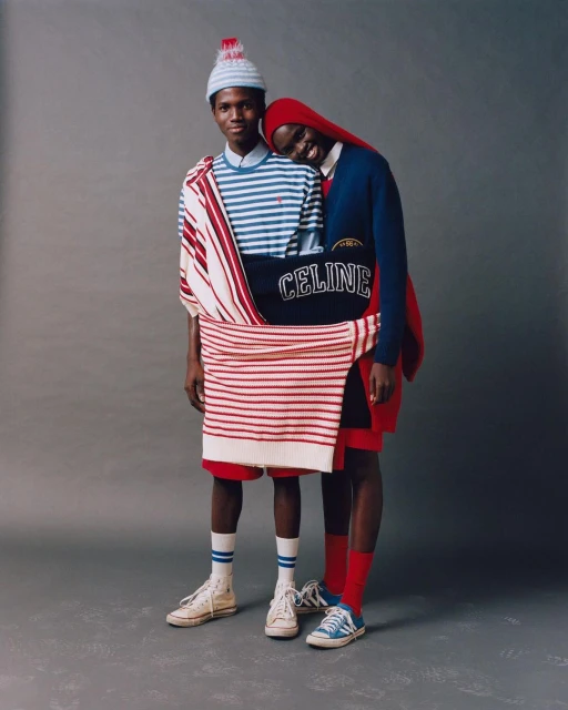 Two dark-skinned adults in red, white, and blue apparel and vintage sneakers pose in a studio for a fashion editorial.