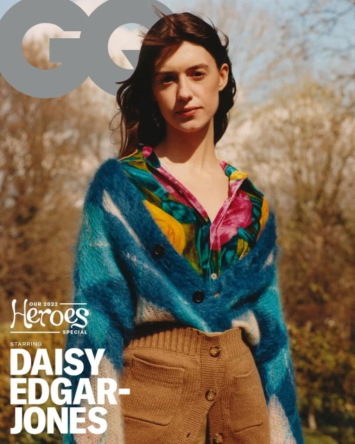 Daisy Edgar-Jones wearing a colorful cardigan and high-waisted shorts, posing for a magazine cover in a blurred outdoor setting.