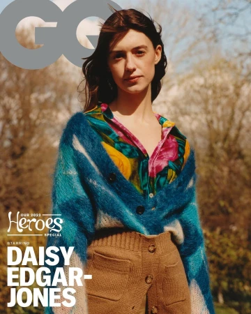 Daisy Edgar-Jones wearing a colorful cardigan and high-waisted shorts, posing for a magazine cover in a blurred outdoor setting.