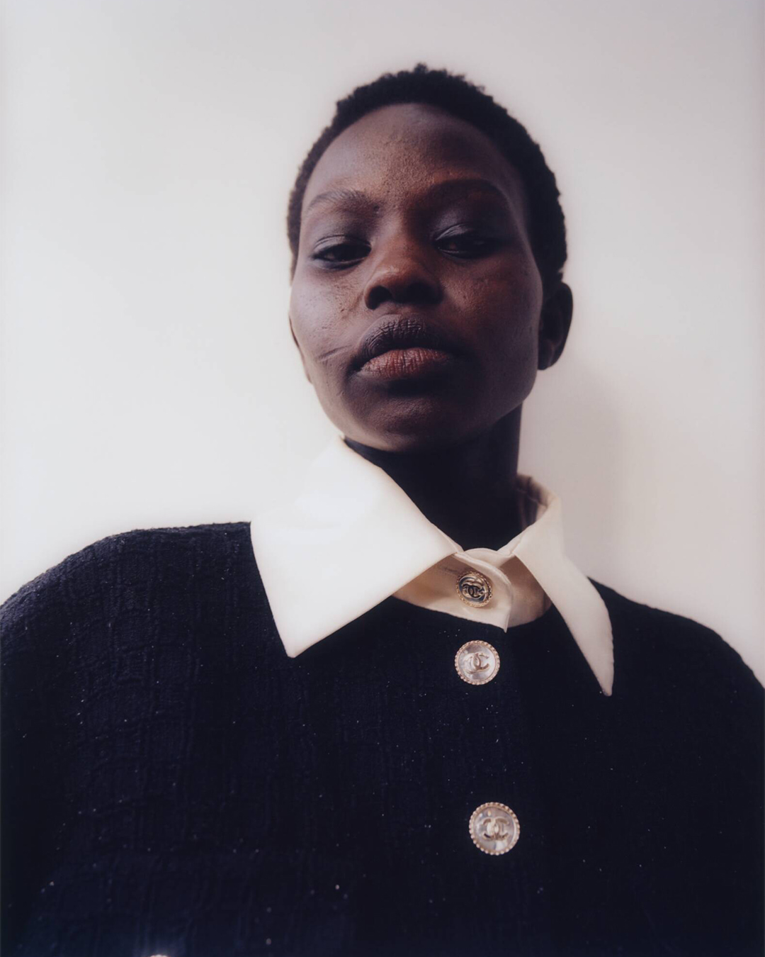 Headshot of a Black woman wearing a black jacket with a white collar and silver buttons against a plain, neutral background.