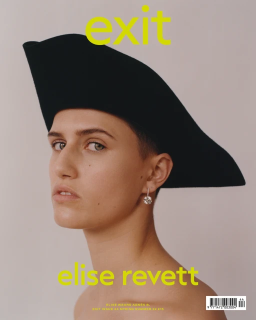 Magazine cover featuring a woman with short hair wearing a large black hat and dangling earrings against a muted background.
