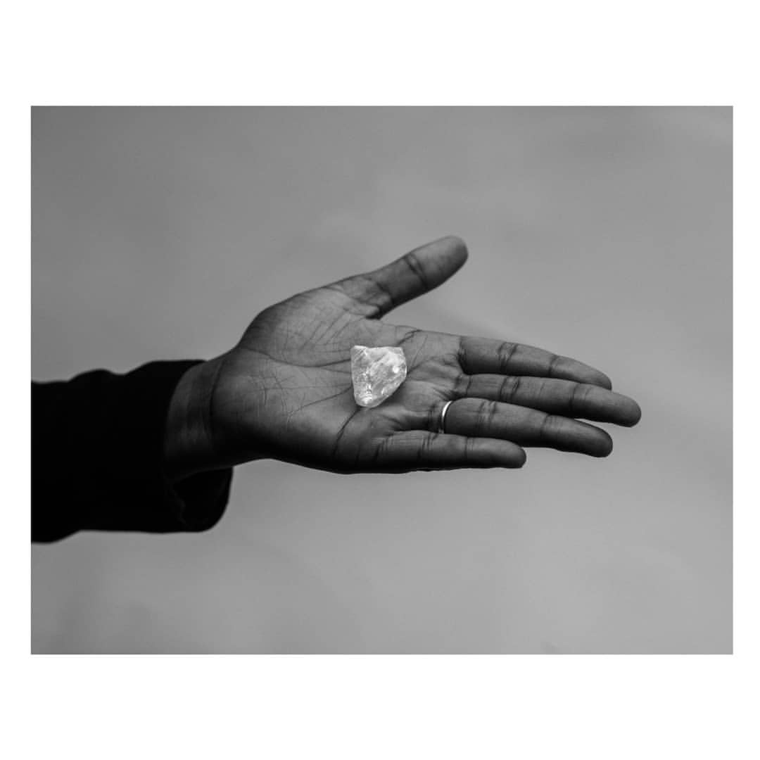 Person holding a clear crystal in their open palm against a grey backdrop, showing the stone's details and light reflection.
