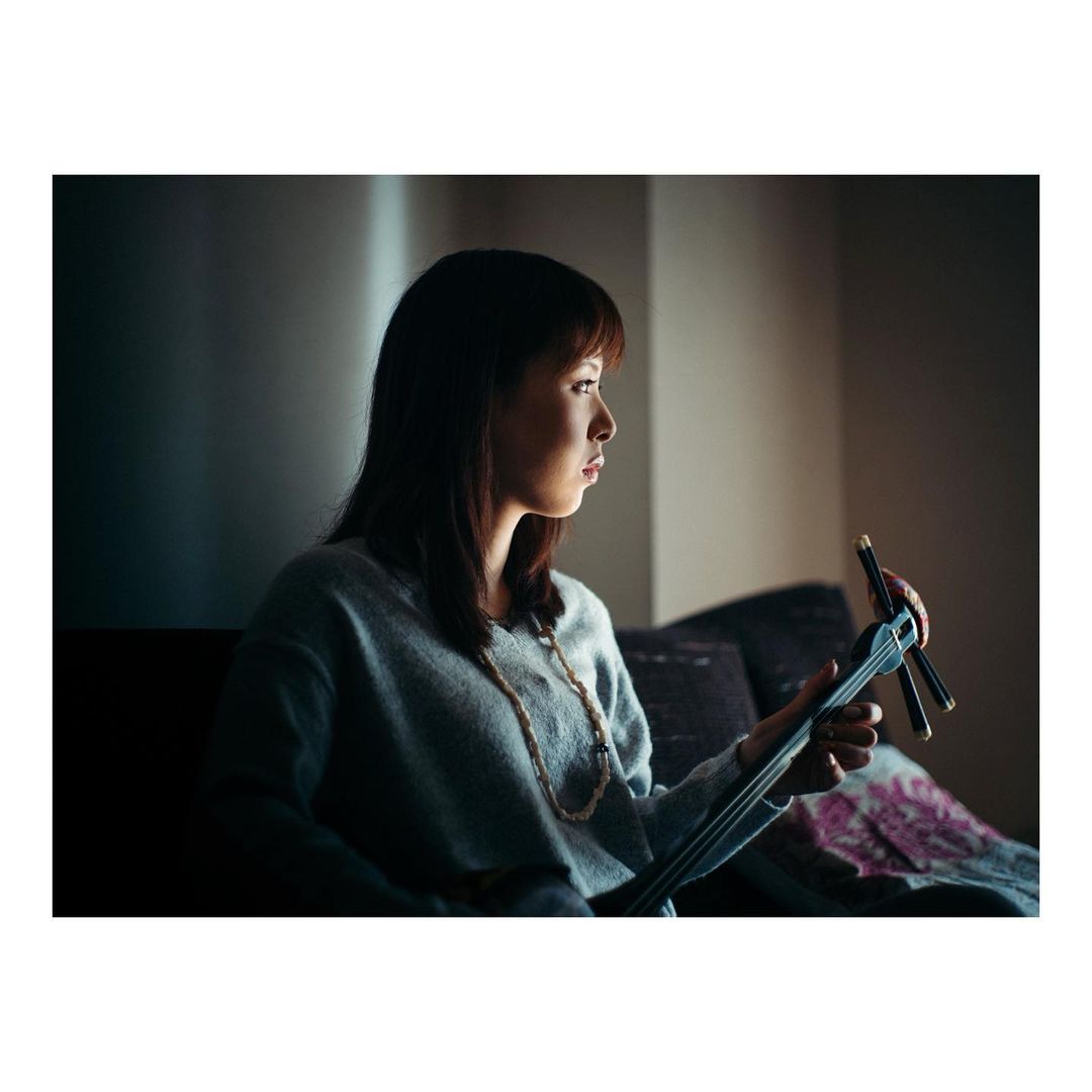 Portrait of a woman playing a stringed instrument indoors, illuminated by natural light, creating a focused and serene atmosphere.