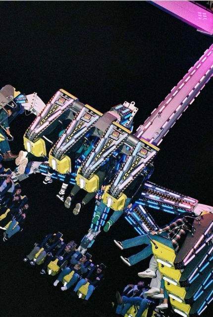 People on a thrilling amusement park ride at night, captured from a high angle with vibrant lights and dynamic motion, creating a sense of excitement.