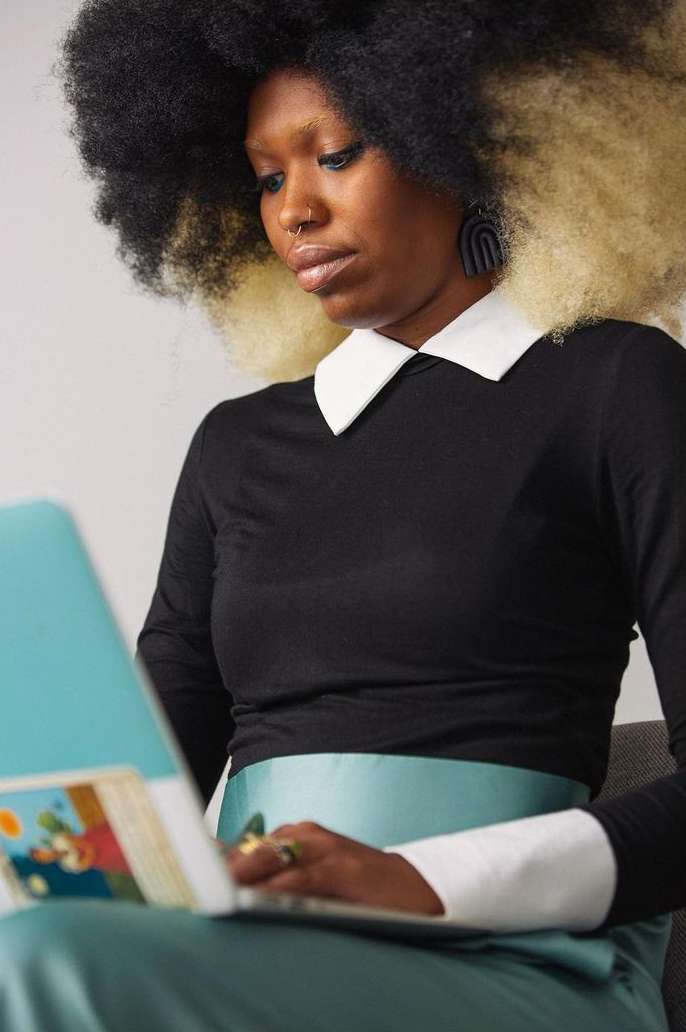 Black woman with afro hairstyle and black top with white collar working on a laptop. Indoor shot. Focus on the model.