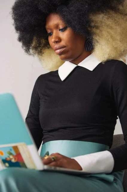 Black woman with afro hairstyle and black top with white collar working on a laptop. Indoor shot. Focus on the model.