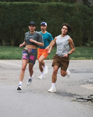 Three people running outdoors on a paved surface with green foliage in the background.  Runners are wearing athletic clothing and sneakers.