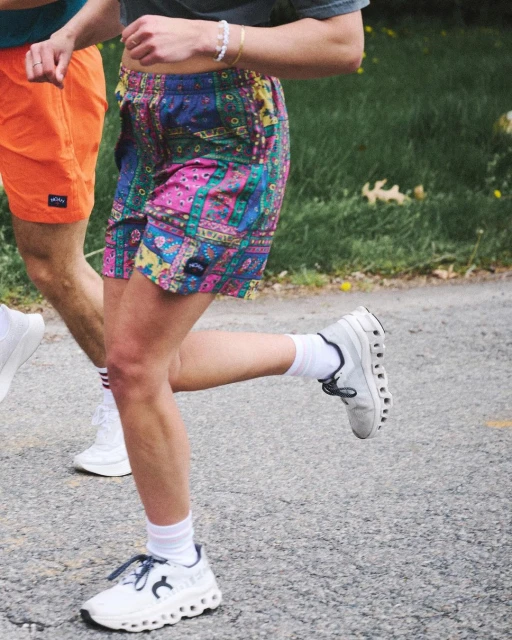 Two people jogging outdoors on a paved surface wearing colorful patterned shorts and athletic shoes with green foliage visible. 