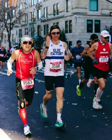 Marathon runners compete on a city street. Athletic men in sportswear run, buildings and trees are in the background.