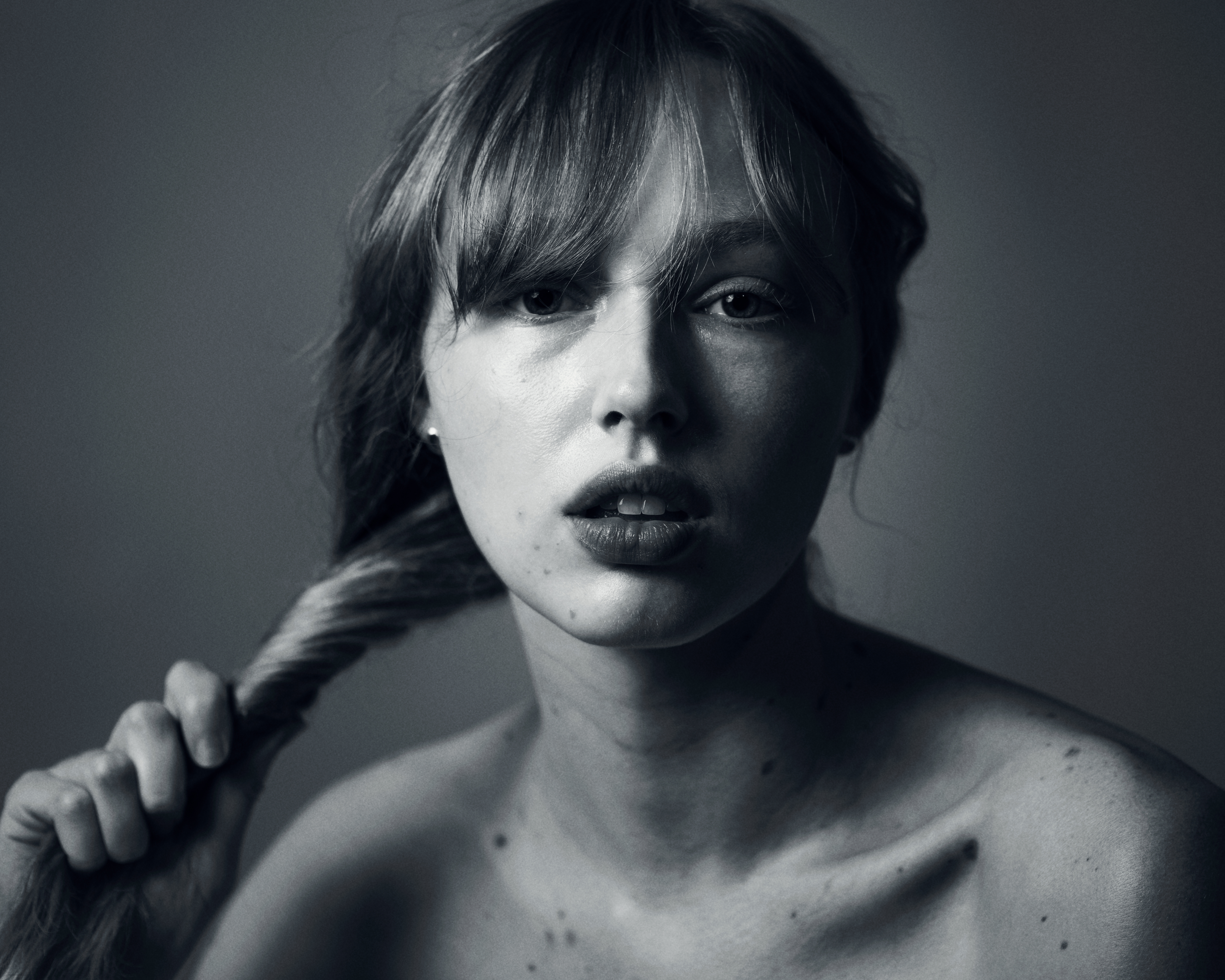 Portrait of a young adult female with fair skin, light brown hair, a braid, and neutral expression, against a grey backdrop.